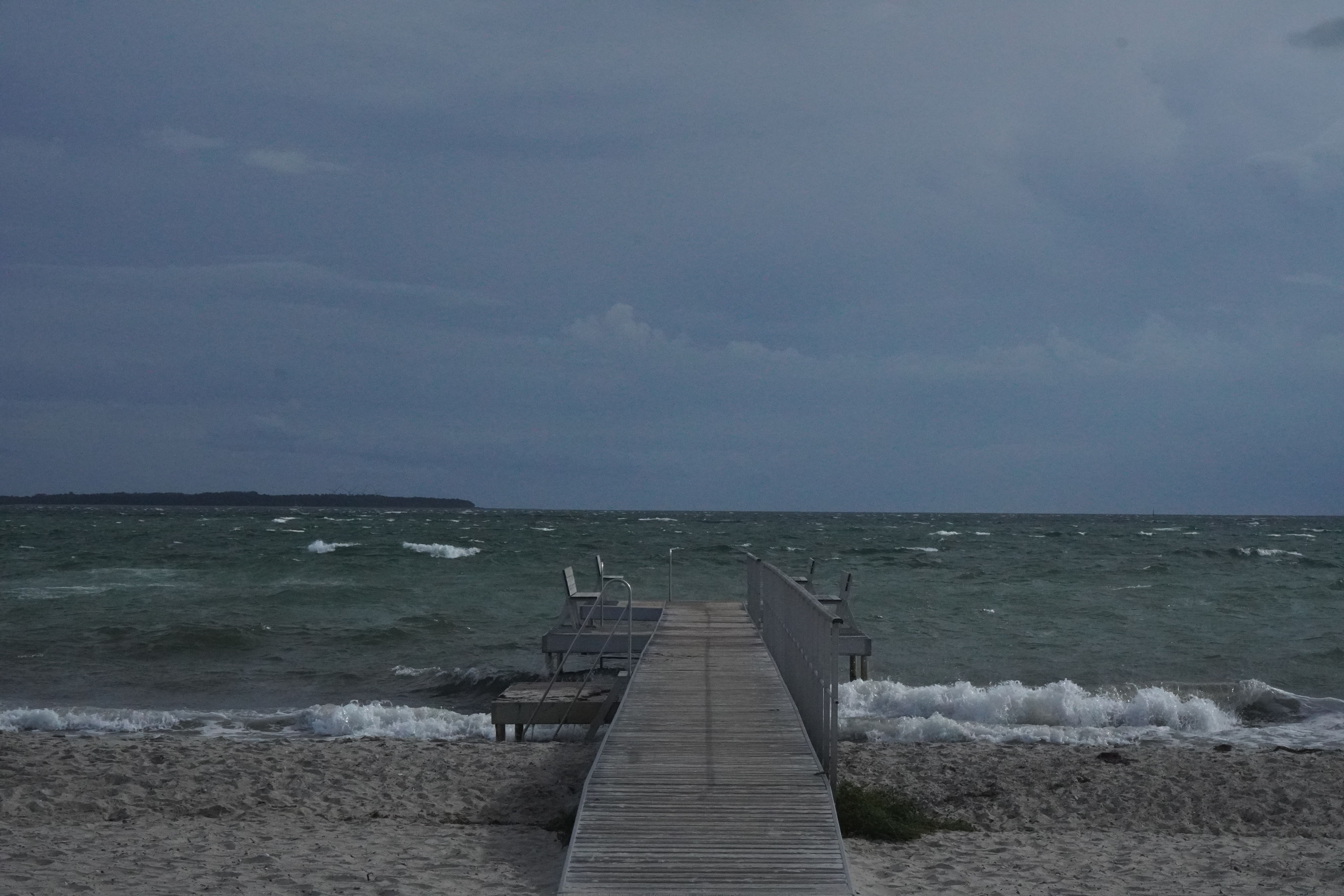Blæsende dag ved stranden med badebro og bølger