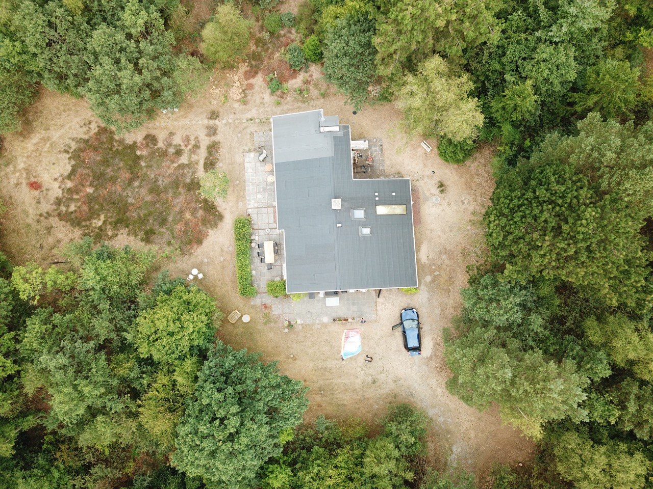 Topdown-luftfoto af sommerhusets tag, terrasse og skovgrund